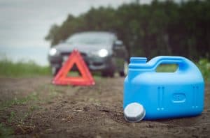 A blue fuel canister sits on the ground near a dirt road, with a red warning triangle and a blurred car in the background, hinting at a car breakdown and the need for roadside assistance in Maricopa County, AZ.
