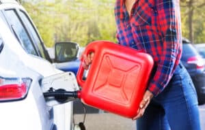 A person in a plaid shirt refuels a white car with a large red gasoline canister near the open fuel tank outdoors, showing typical roadside assistance in Maricopa County, AZ.