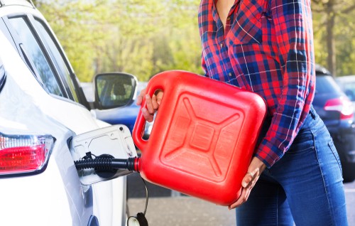 A person in a plaid shirt refuels a white car with a large red gasoline canister near the open fuel tank outdoors, showing typical roadside assistance in Maricopa County, AZ.