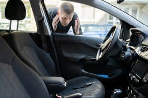 A man in AZ looks anxiously through the window of a parked car, hands raised to his face, after spotting car keys left on the driver’s seat—locked inside and in need of roadside assistance Maricopa County can depend on.
