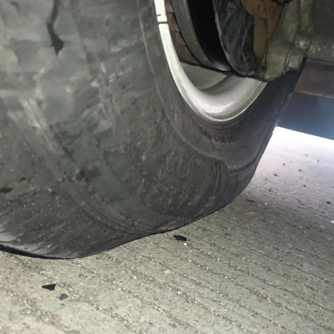 A close-up of a car tire that is extremely worn out and flat, with the wheel rim nearly touching the ground on a concrete surface, highlighting the urgent need for roadside assistance in Maricopa County, AZ.