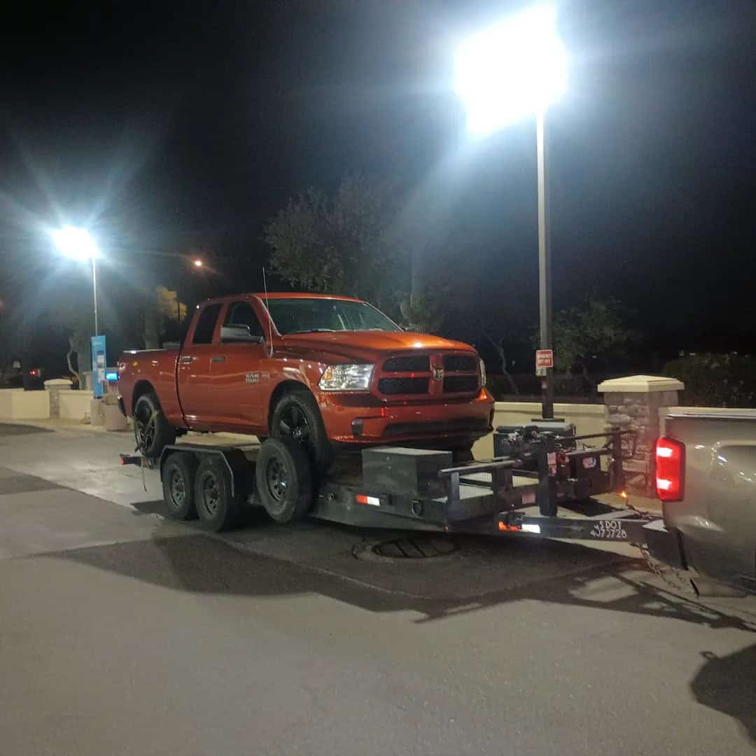 A red pickup truck is loaded onto a flatbed trailer, being towed at night under bright streetlights in a Maricopa County parking lot, showcasing AZ roadside assistance in action.